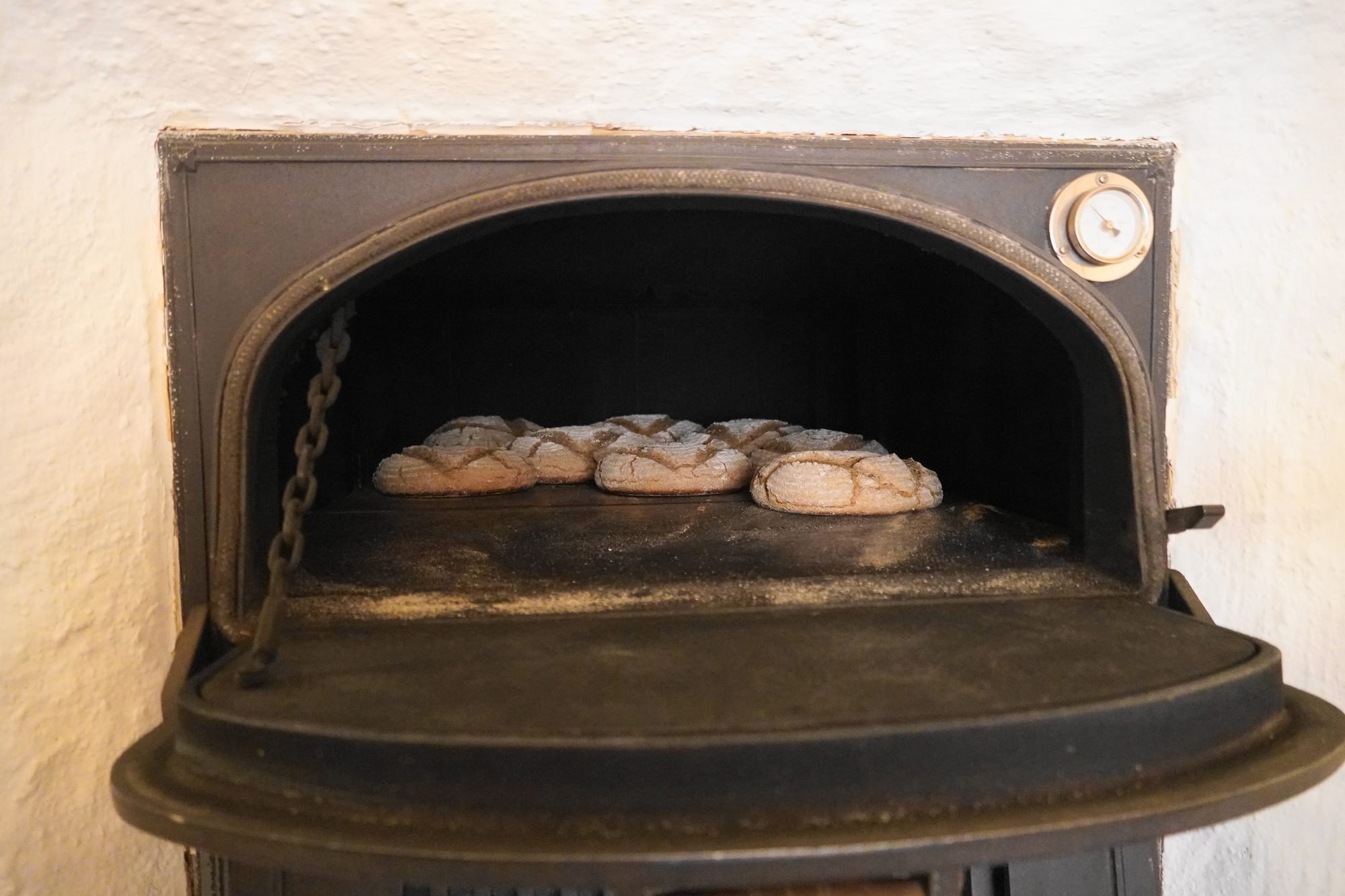 Loaves baking inside a cast-iron wood oven, its door open