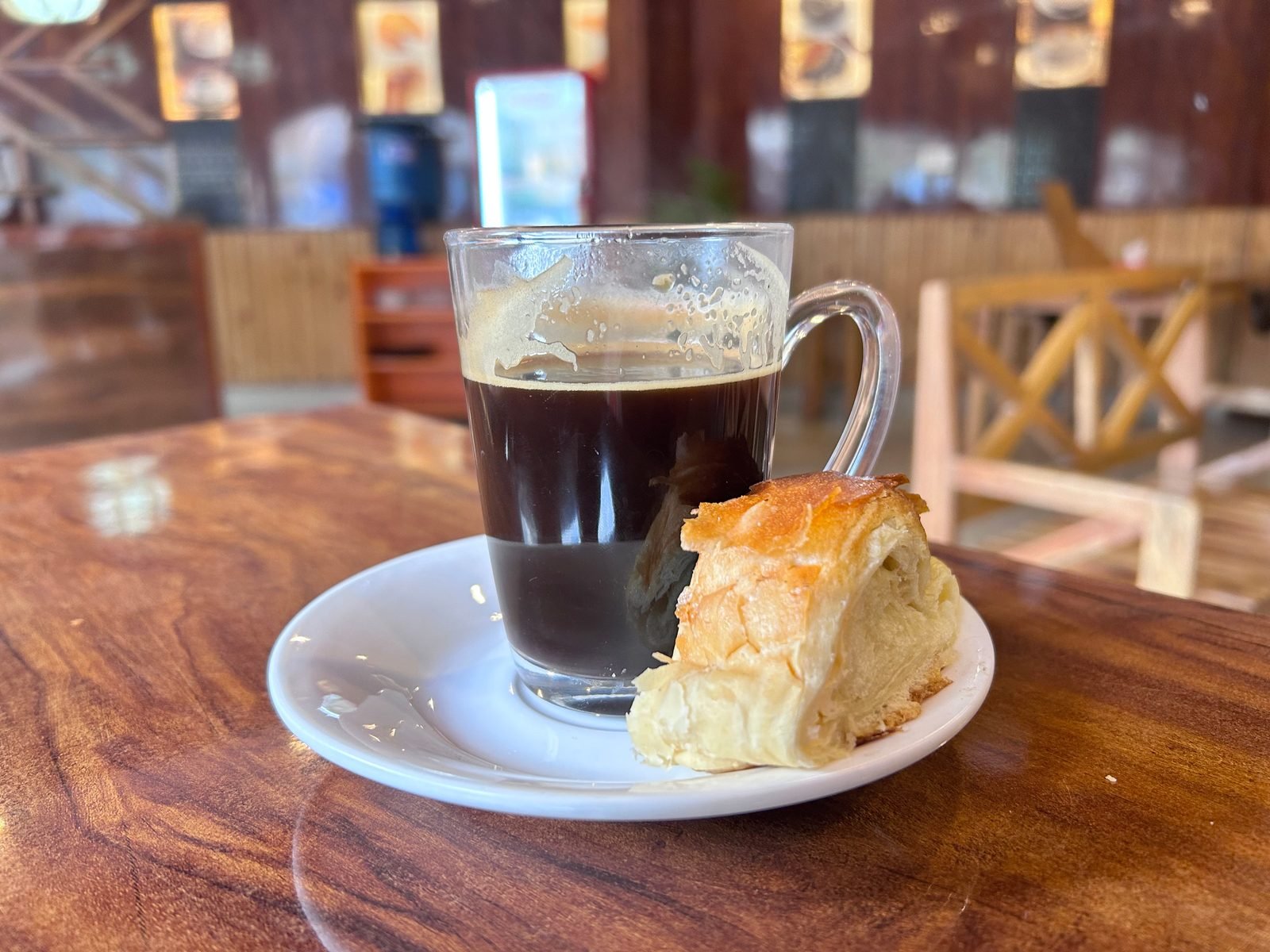 A glass of black coffee beside a pastry