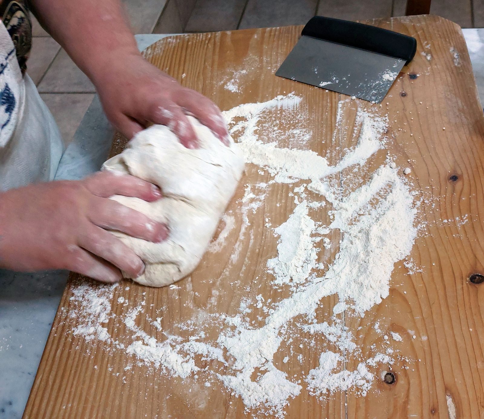 Hands kneading dough on a floured wooden board
