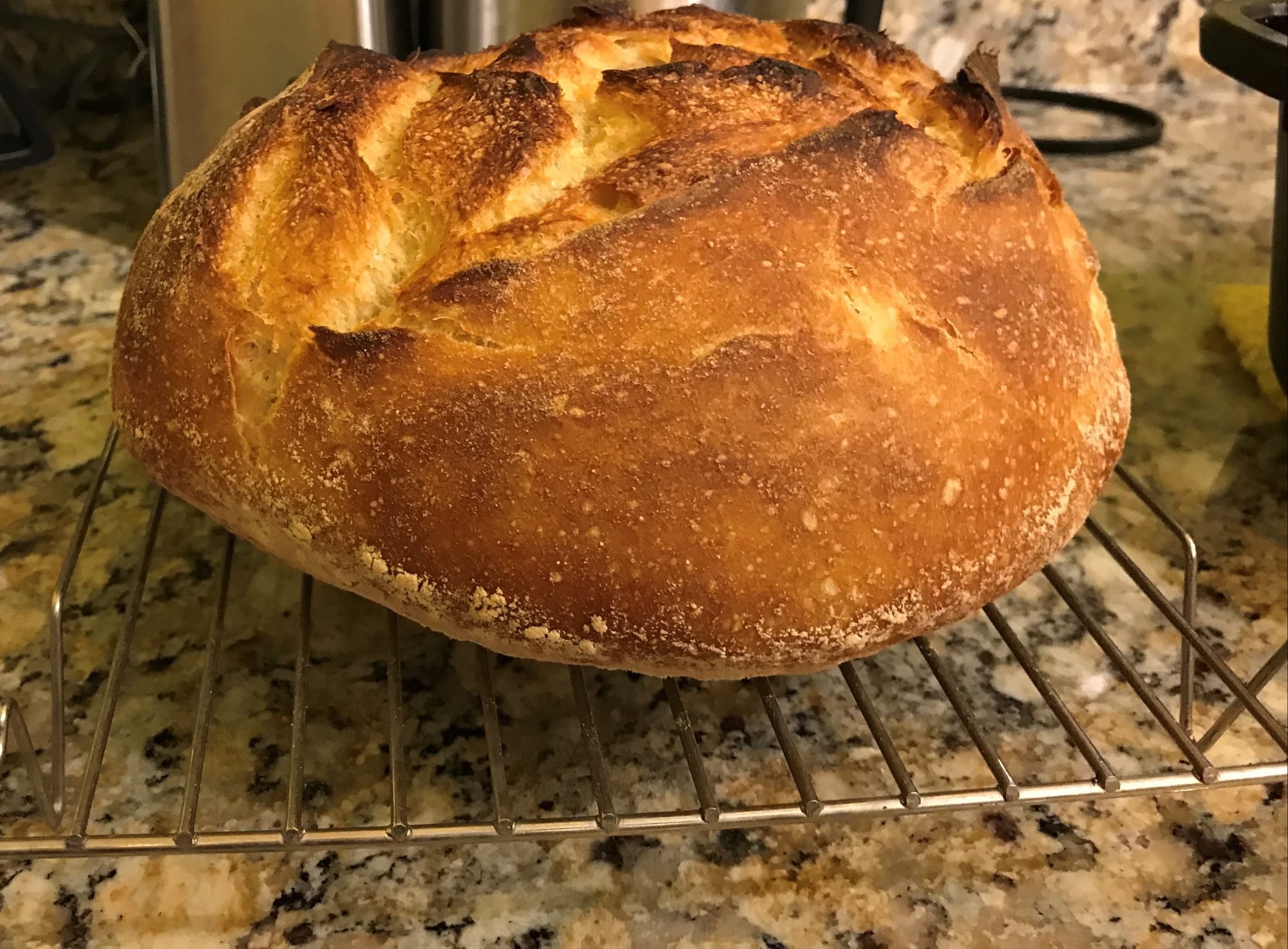 A round sourdough loaf with a golden, cracked crust on a cooling rack
